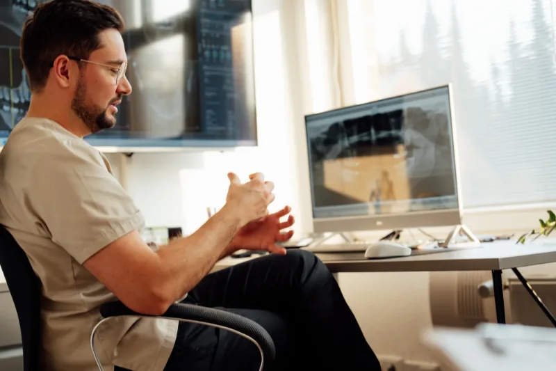 Dmitri Klass in the consultation room, explaining 3D X-ray images shown on the screens behind him
