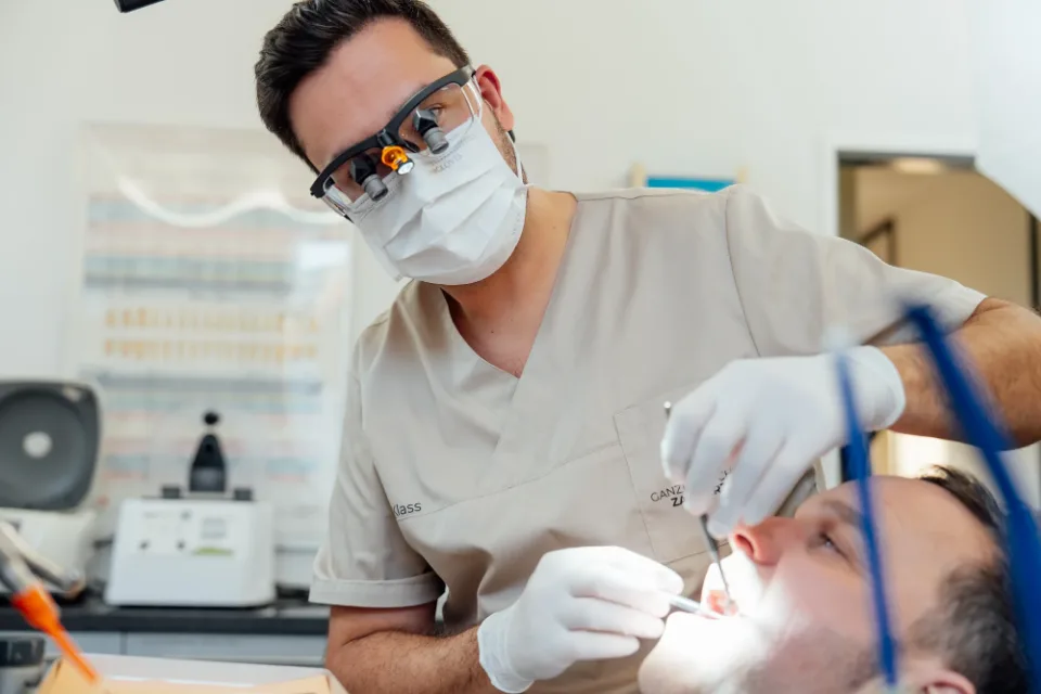 Dmitri Klass treating a patient at the chair, wearing magnifying loupes